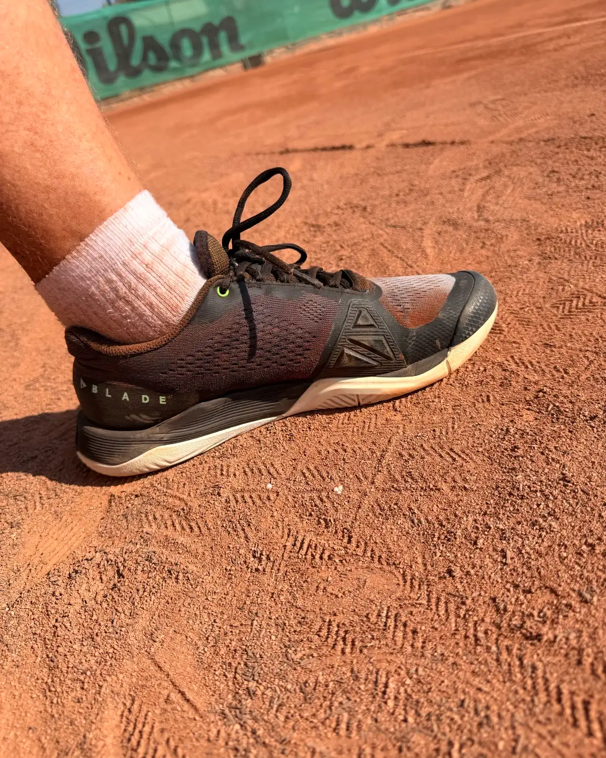 A clay-court shoe on the red dirt, mid-changeover